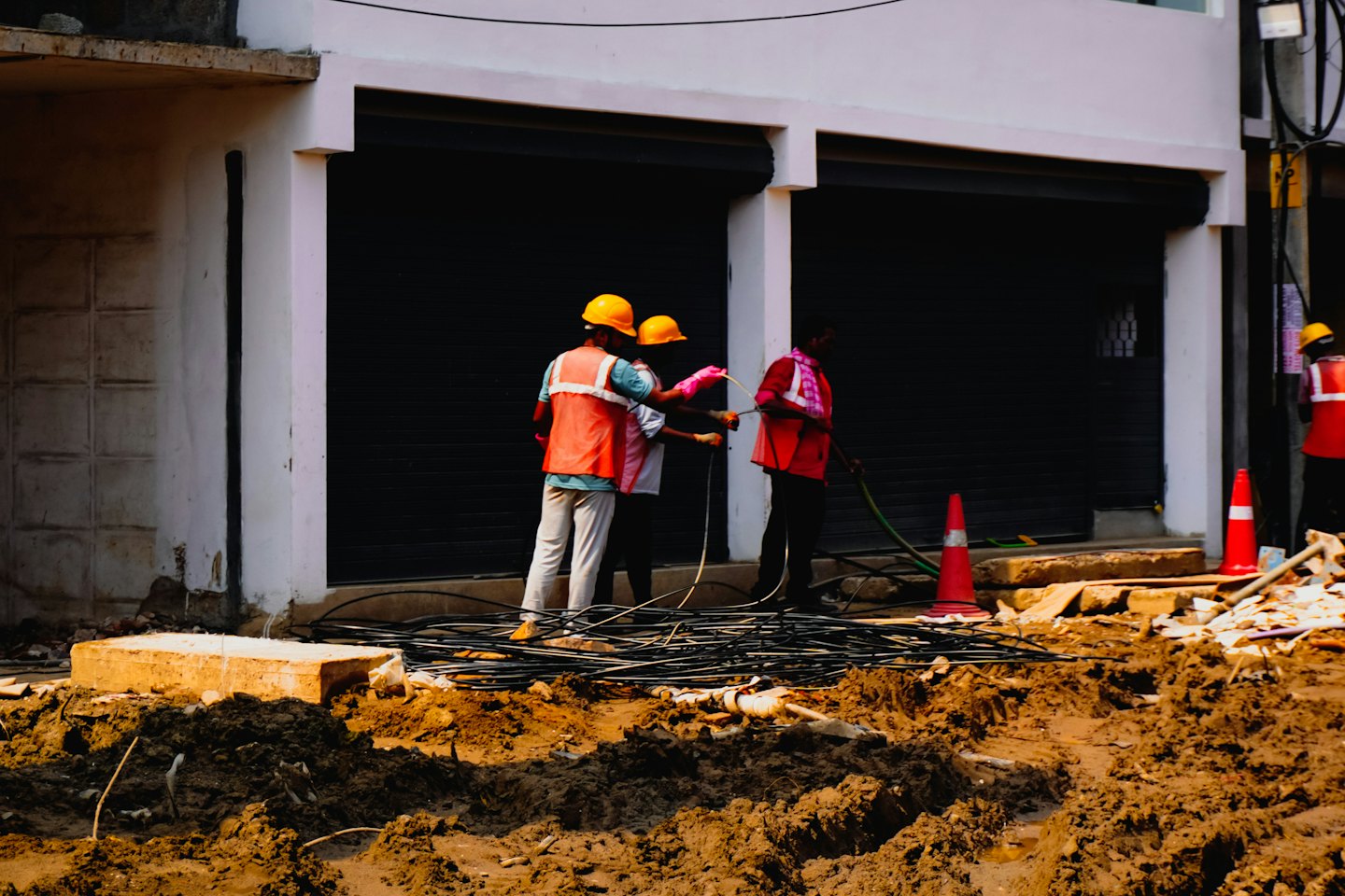 Tres trabajadores de servicios públicos manejan cables eléctricos en una obra.