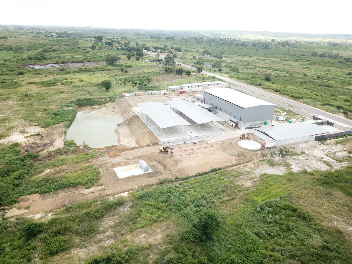 Vehículos de construcción trabajan cerca de edificios industriales nuevos y un estanque.