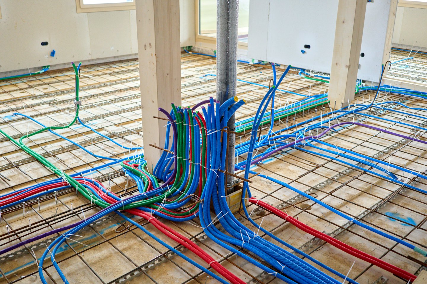 Tuberías de fontanería y conductos eléctricos de colores sobre un subsuelo de construcción.