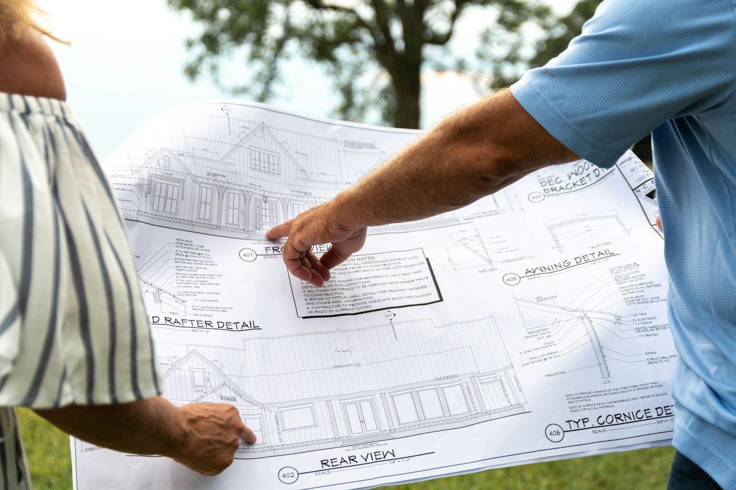 Dos personas discuten planos arquitectónicos de casas al aire libre.