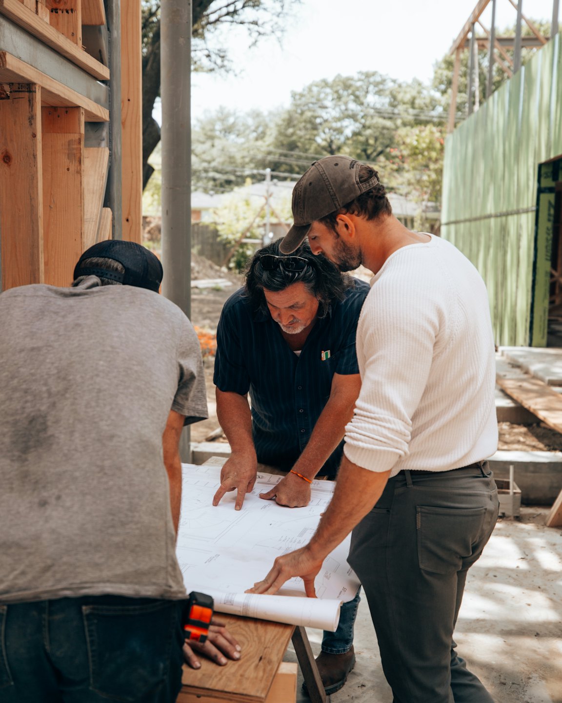 Tres profesionales de la construcción revisan planos en una obra al aire libre.