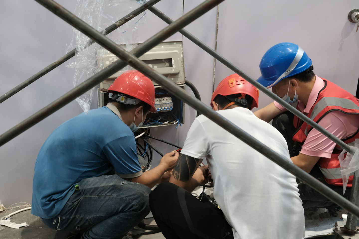 Hombres con casco conectan cables a un panel eléctrico en interiores.