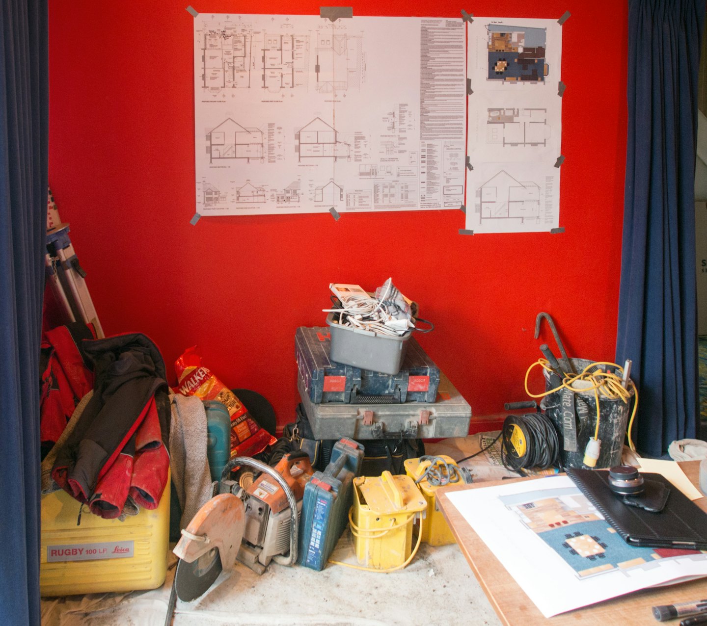 Planos arquitectónicos y herramientas de construcción esparcidos por una obra en renovación.